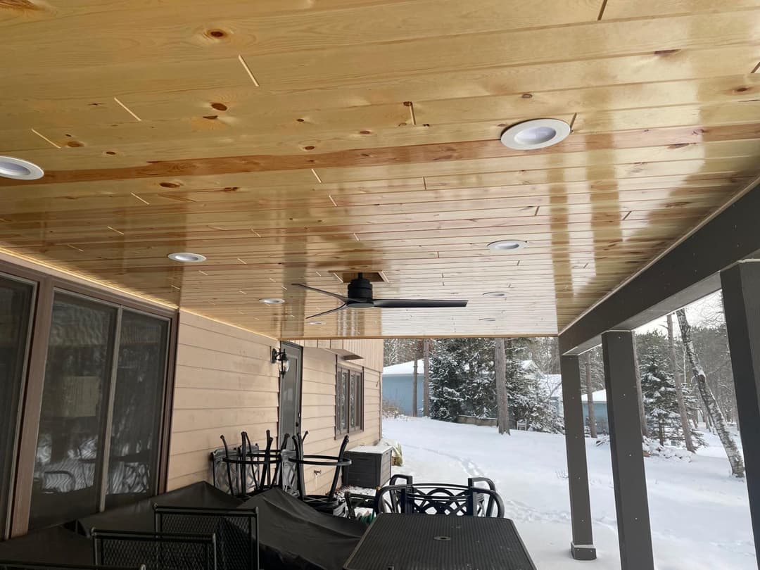 Outdoor wood ceiling with recessed lighting and a ceiling fan installed above a patio.