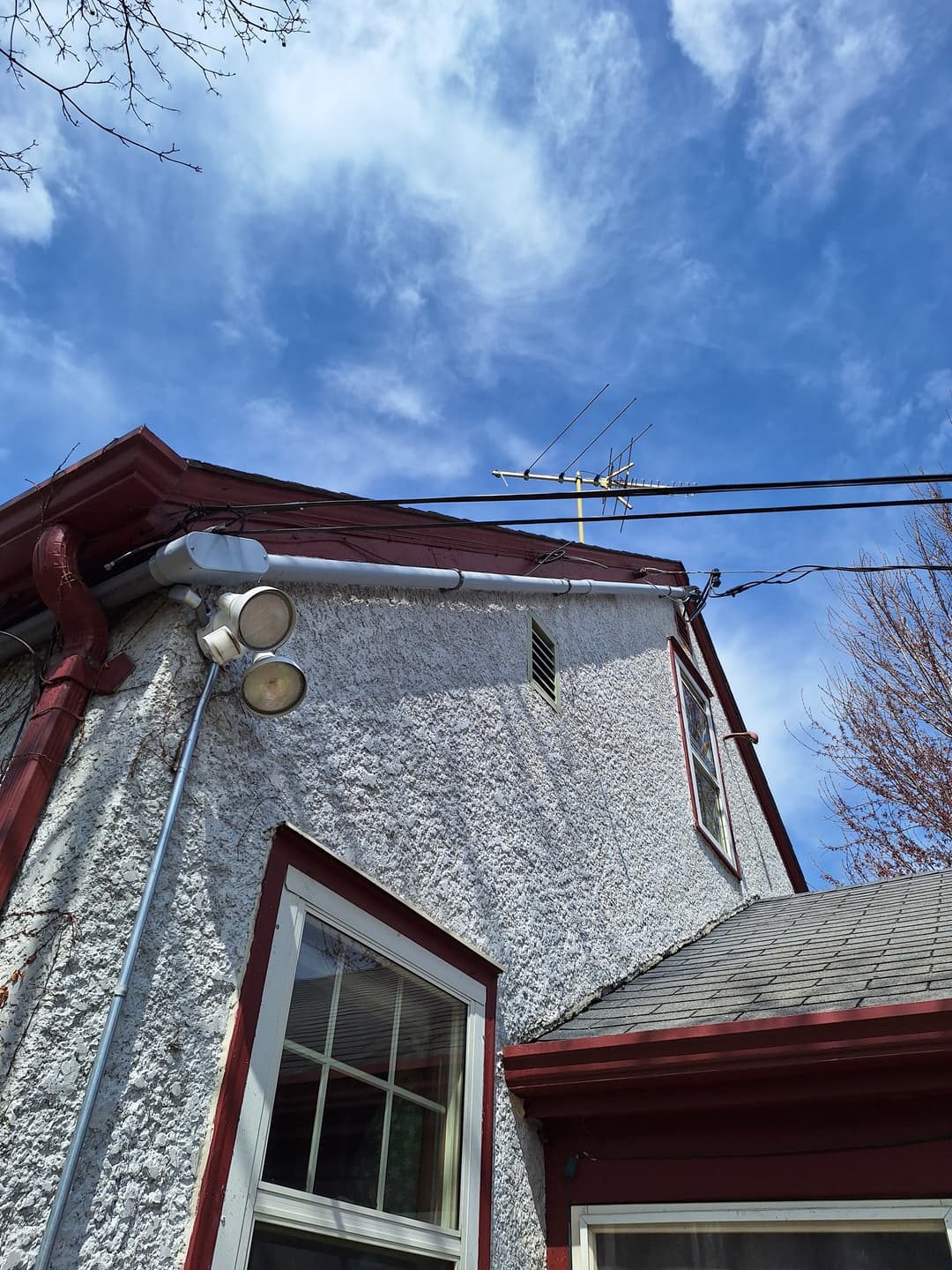 Exterior overhead service mast and conduit on stucco home with security lights.