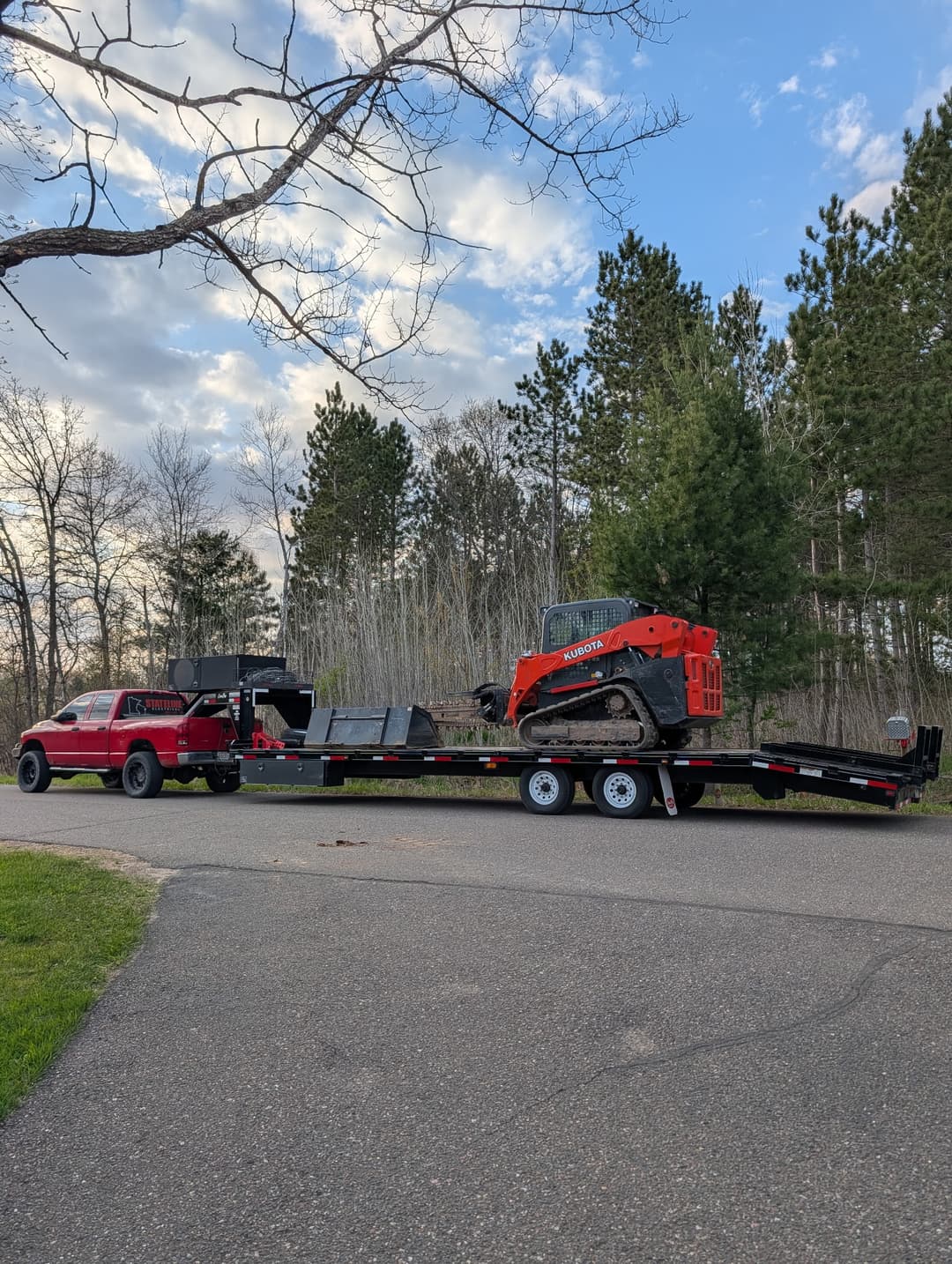 Stateline Electrical branded pickup truck towing a trailer with a Kubota skid steer to a rural jobsite in Minnesota.