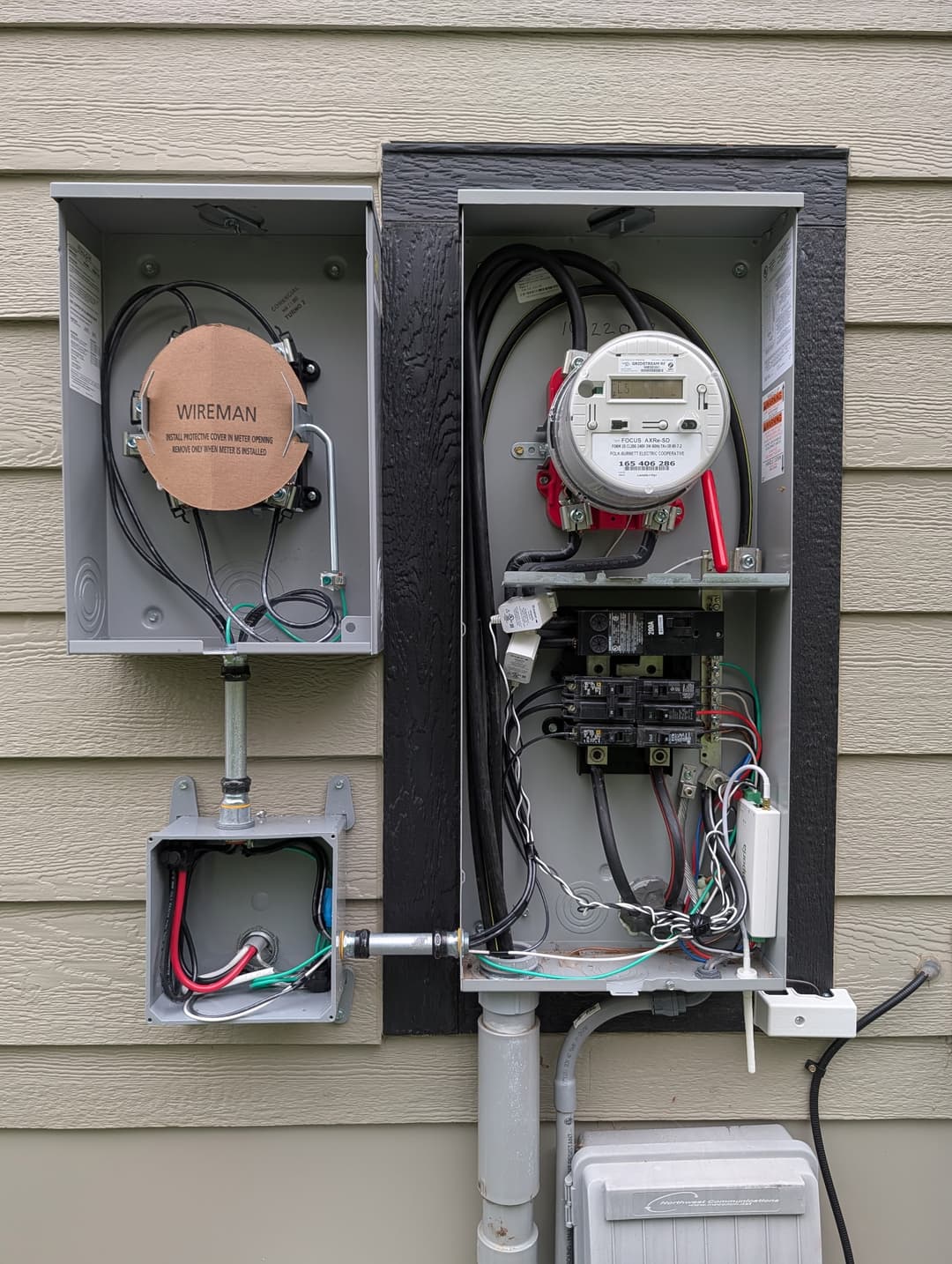 Dual electrical meter sockets and 200A service panel installed on residential siding with organized conduit.