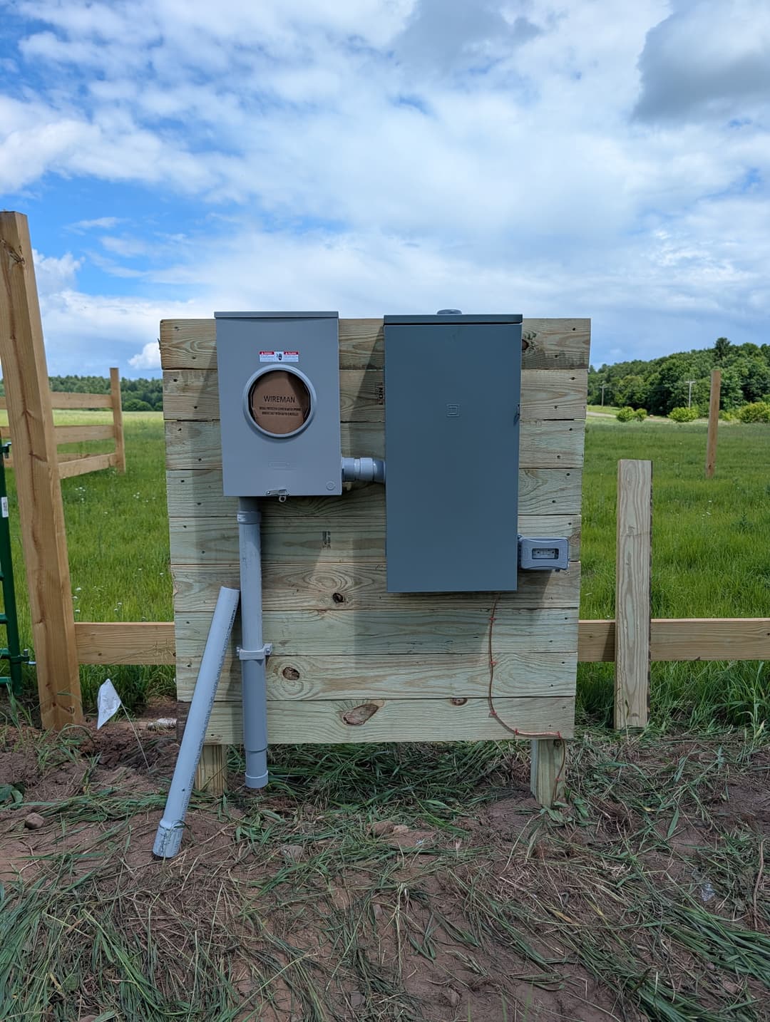 Electrical meter and breaker panel installed on a wood-mounted service stand in a rural Minnesota field.
