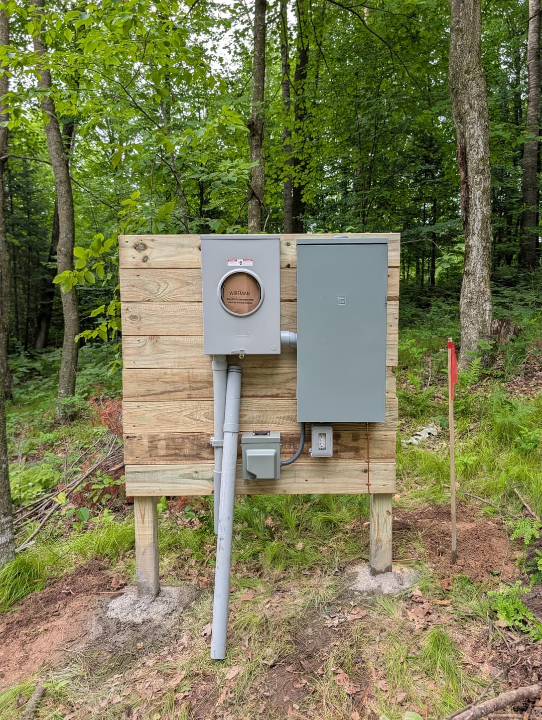 Meter socket and Square D panel mounted on a wood post stand for new electrical service on a wooded rural property.