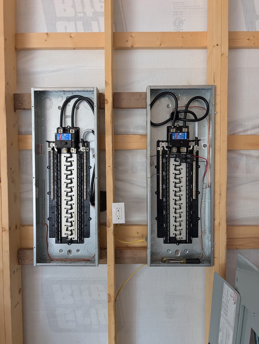 Two electrical panels installed in a home under construction, showing breakers and organized wiring during rough-in.