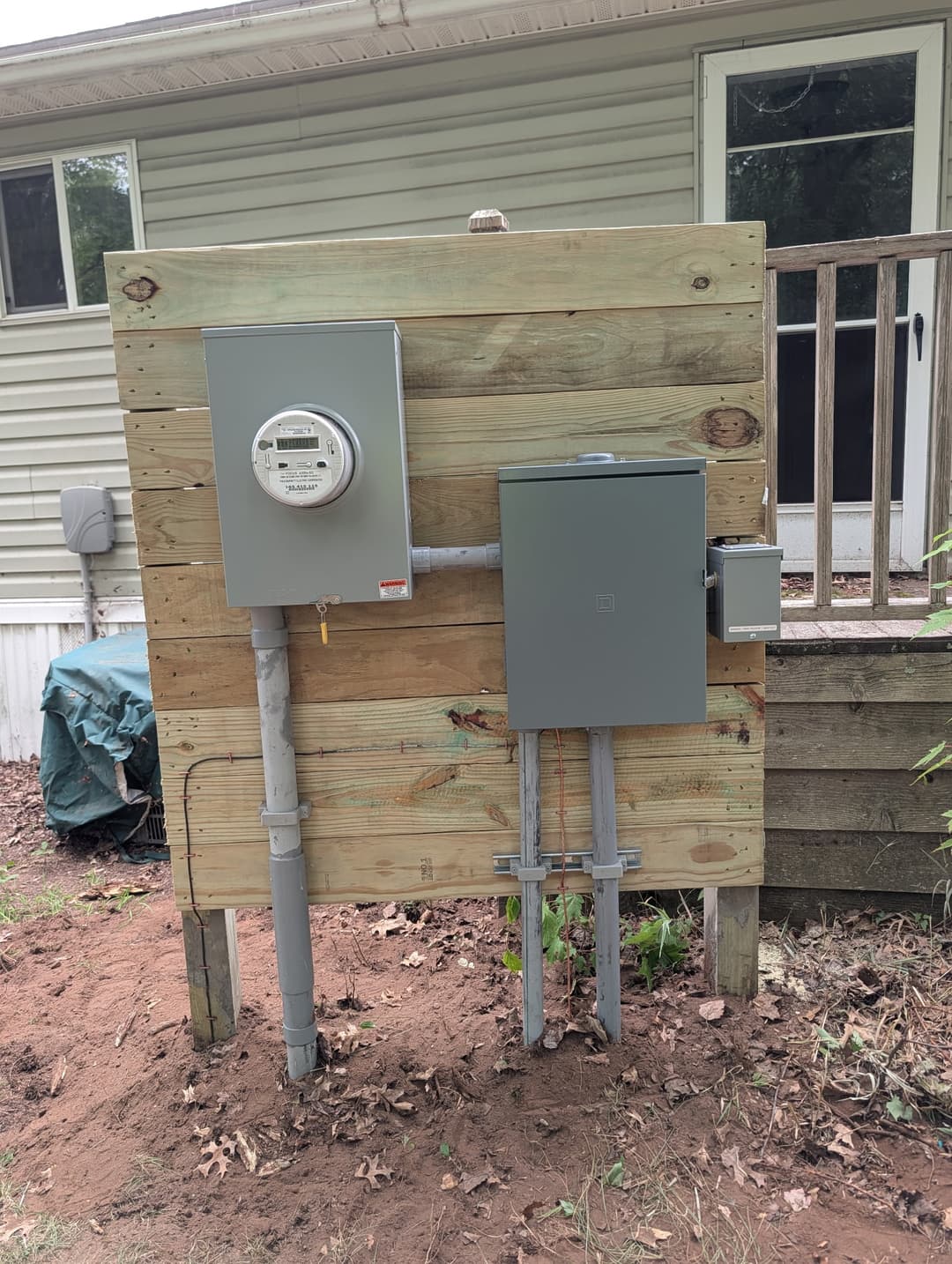 Electrical meter and 200A panel installed on a wood backboard behind a Minnesota home.