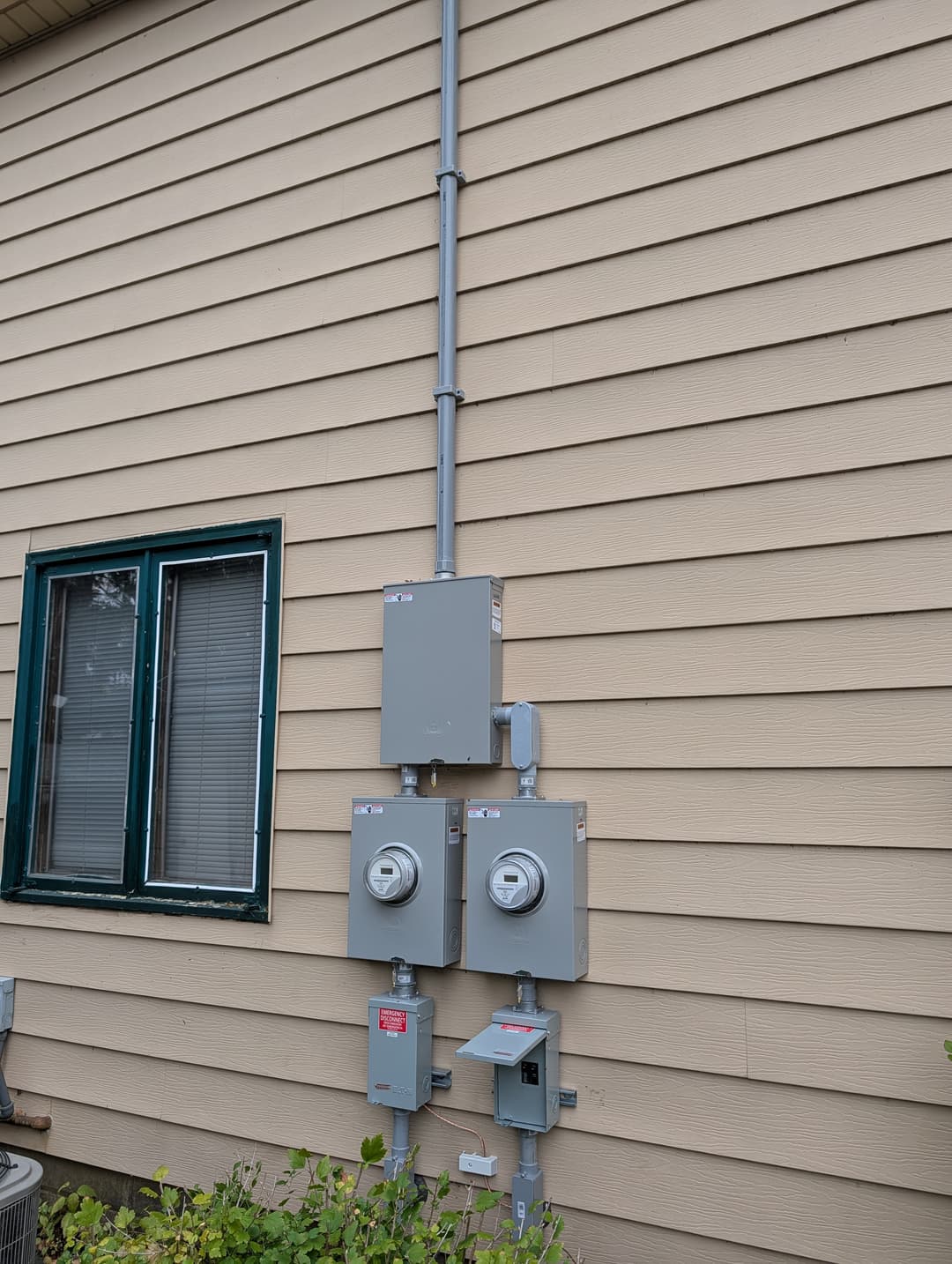 Exterior electrical service installation with dual meters, disconnects, and conduit on tan siding.