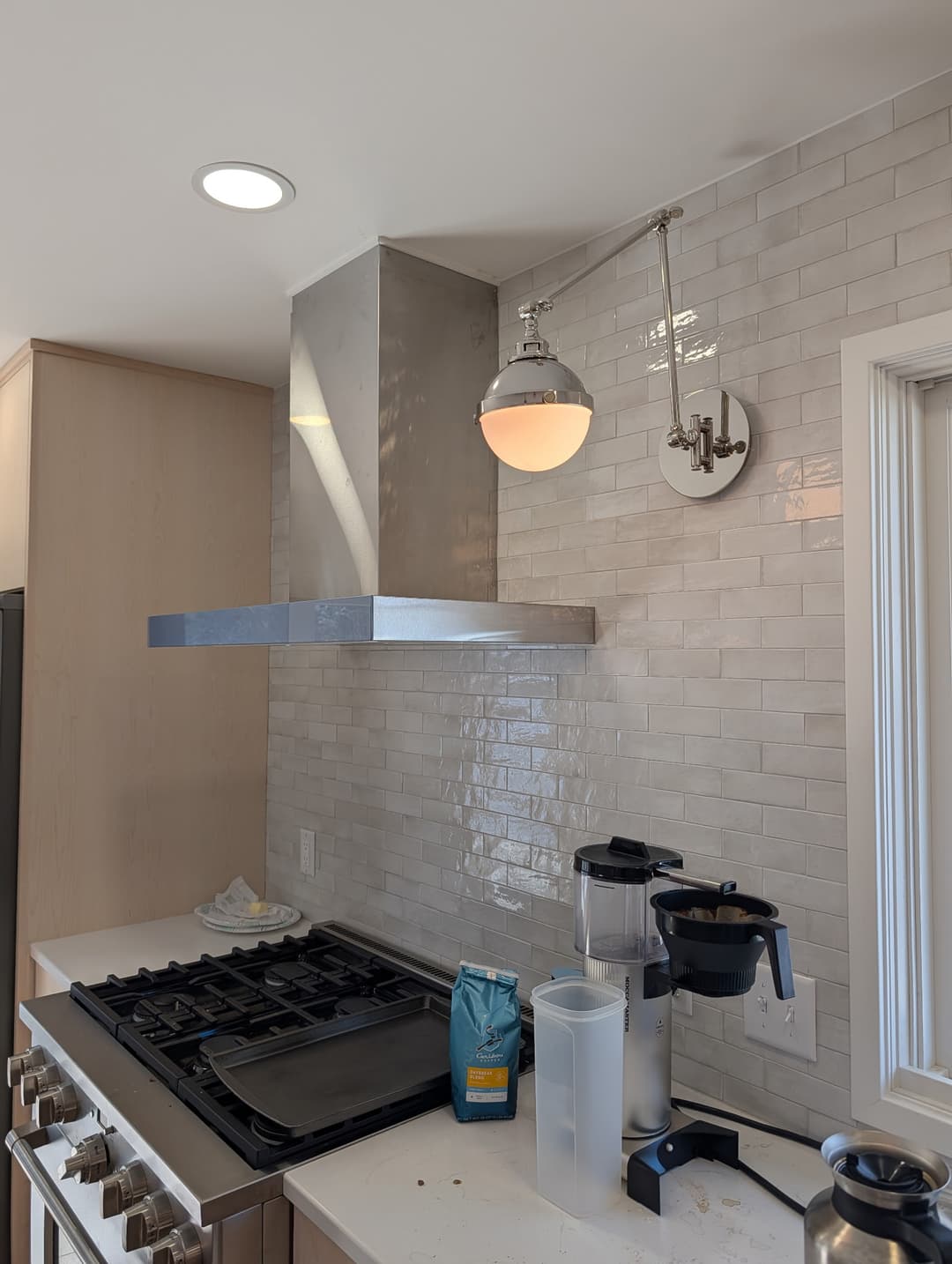 Polished nickel swing-arm wall sconce wired above a tile backsplash next to a stainless steel range hood.