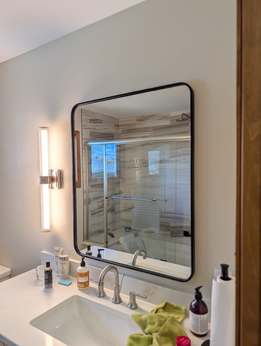 Vertical LED vanity light wired beside a bathroom mirror during a remodel.