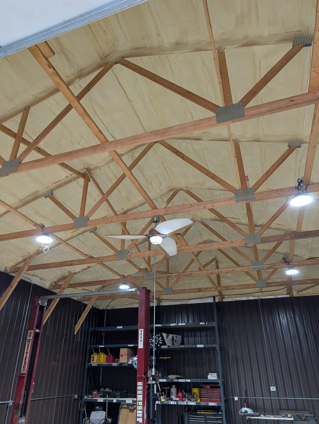 Round LED high-bay lights and a ceiling fan wired into a vaulted garage workshop ceiling.