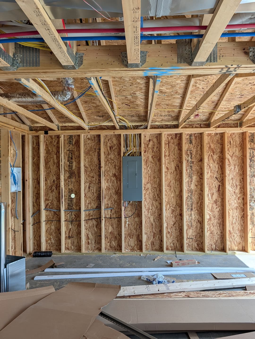 Electrical panel installed in a framed wall with wiring routed through the ceiling during new home construction.