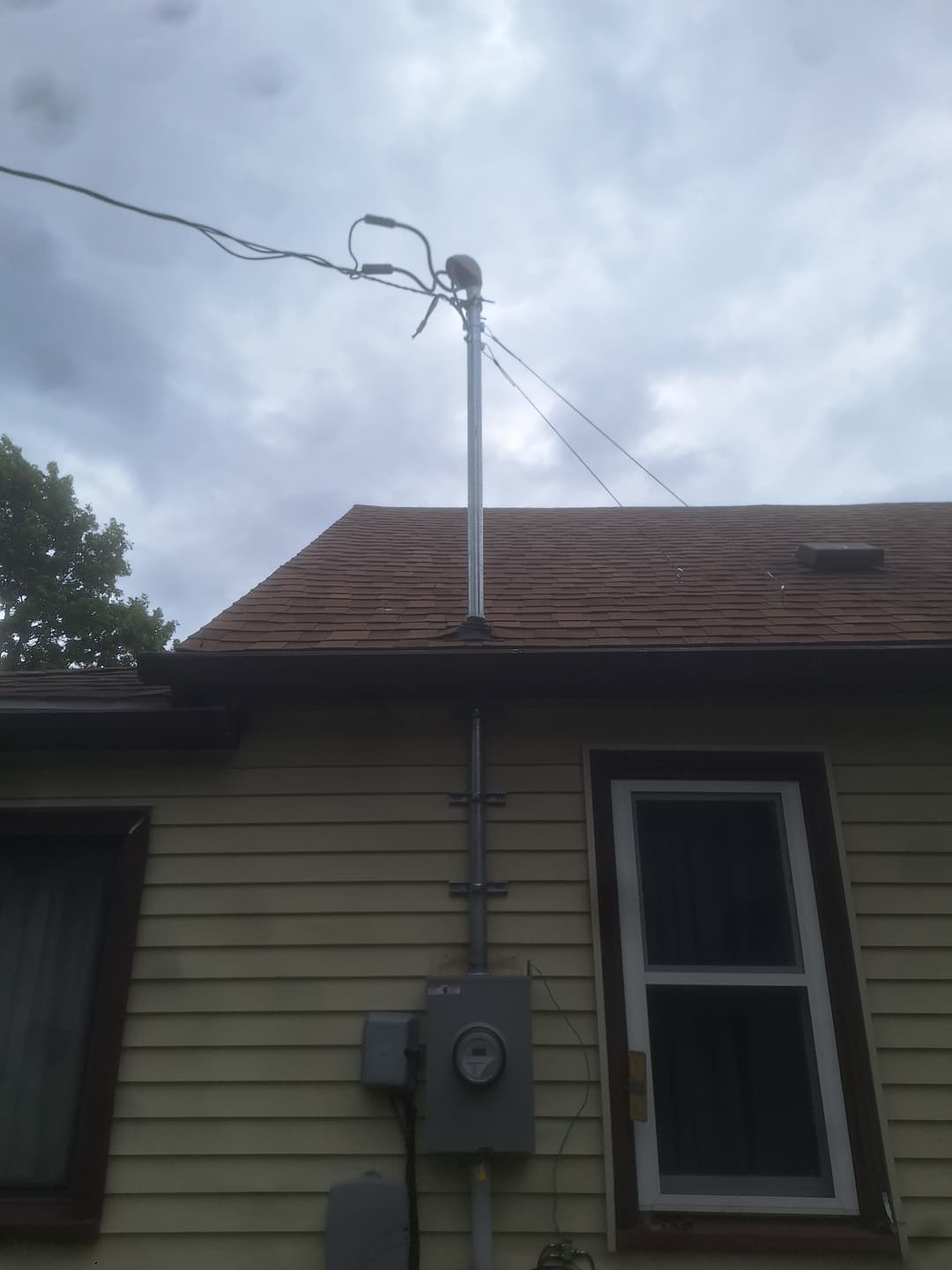 Overhead service mast and exterior electrical meter with conduit on a yellow siding home.