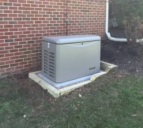 Kohler standby generator installed on a gravel and paver pad against a brick home foundation.