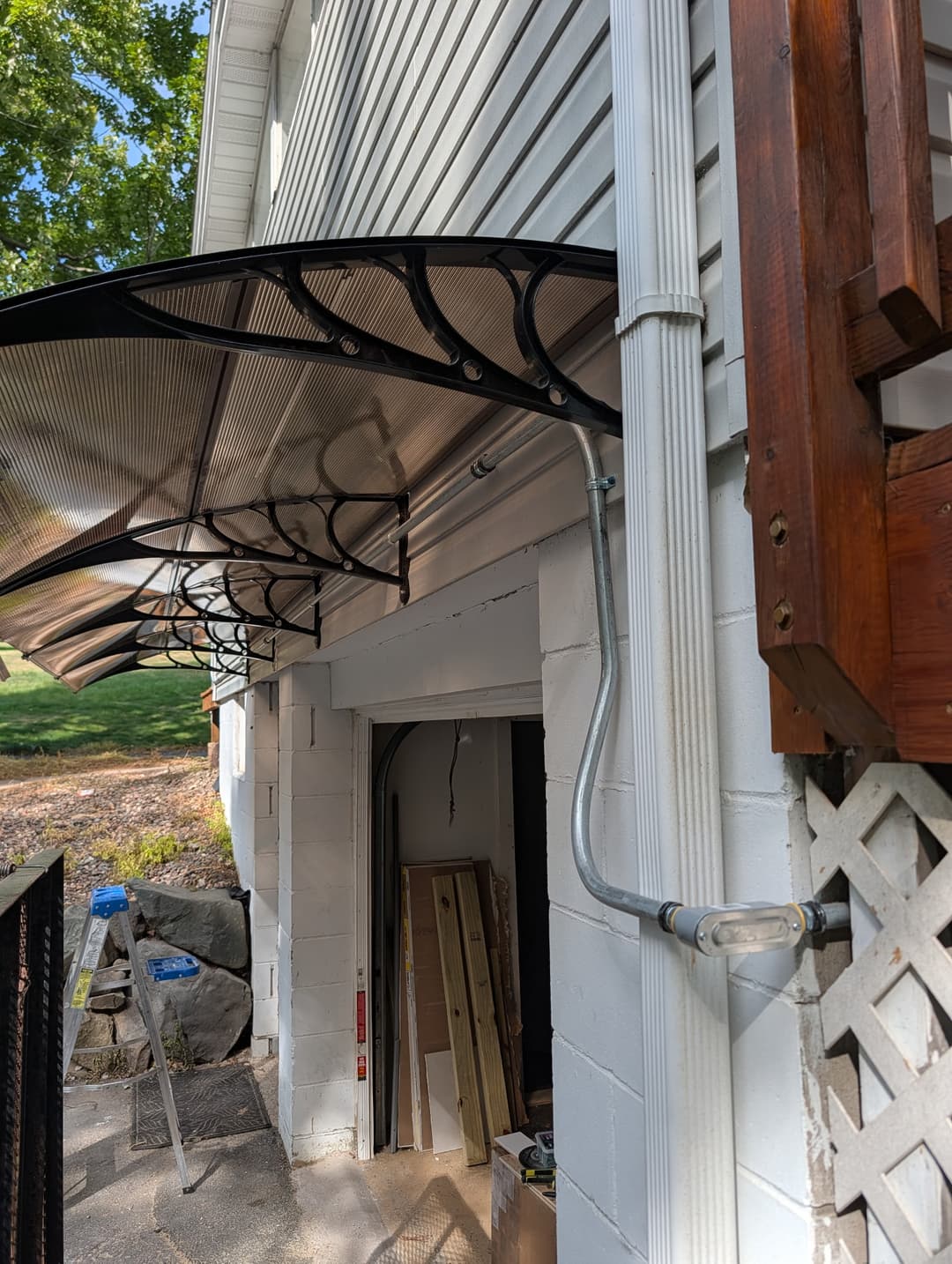 Weatherproof conduit and mast routed along a home exterior beneath a window awning down to a basement service entrance.