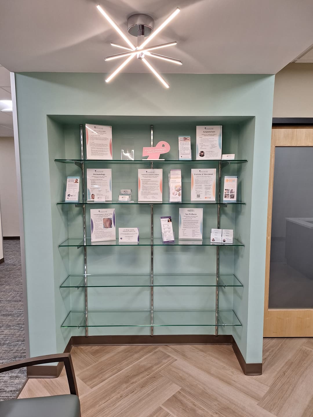 Modern ceiling light fixture installed above glass display shelves in office interior.